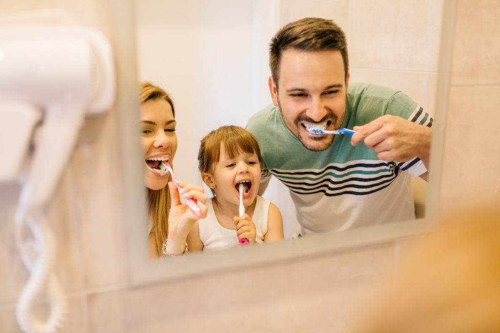 Happy family is brushing their teeth in front of the mirror in bathroom